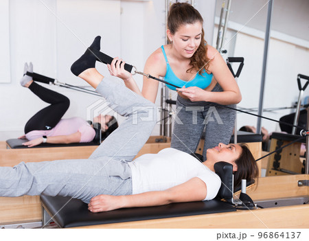 Pilates instructor helping woman exercising on reformer at gym 96864137