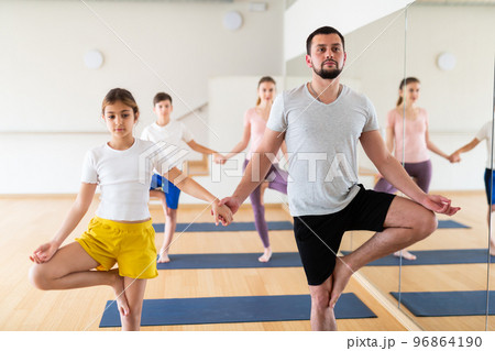 Young girl standing in tree pose with her father during yoga training Young girl standing in tree pose with her father during yoga training 96864190