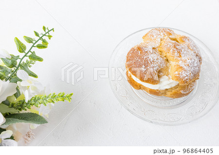Choux Bun with whipped cream and sugar powder on top on plate, white background. Delicate choux pastry dessert. French cream puff. Top view, copy space Choux Bun with whipped cream and sugar powder on top on plate, white background. Delicate choux pastry dessert. French cream puff. Top view, copy space 96864405