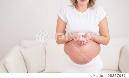 A faceless pregnant woman is holding a handful of white pills. 96867081