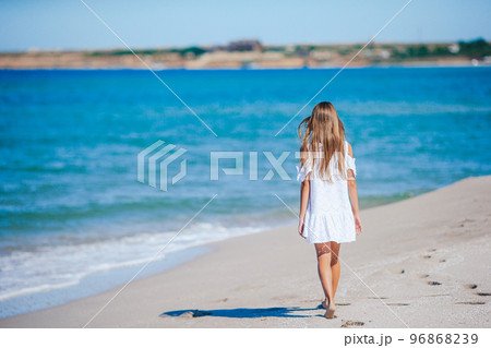 Back view of adorable little girl with long hair in white dress walking on tropical beach vacation Back view of adorable little girl with long hair in white dress walking on tropical beach vacation 96868239