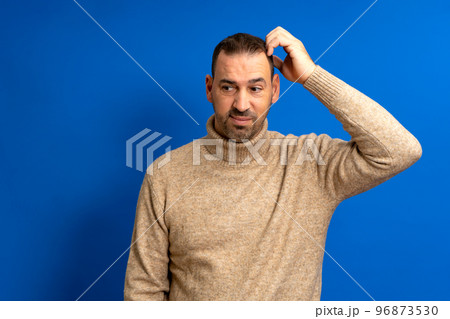 Doubtful bearded latin man thinking, scratching his head and trying to find a solution, isolated on blue background 96873530