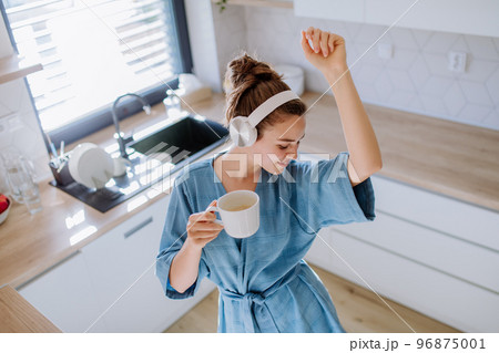Young woman listening music and enjoying cup of coffee at morning, in her kitchen. 96875001