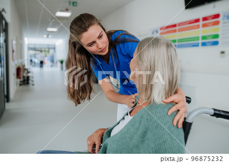 Young woman doctor taking care of senior woman at wheelchair. 96875232