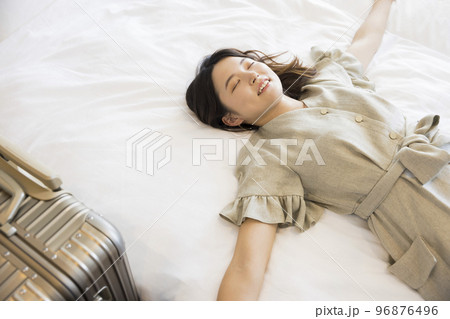 宿泊先のホテルに到着してベッドに寝転がる若い女性の写真素材 [96876496] - PIXTA