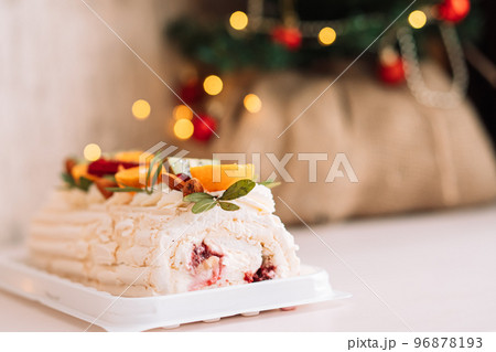 Festive meringue roll with an inscription and decorated with fruits and nuts in front of a Christmas tree and lights from garlands 96878193
