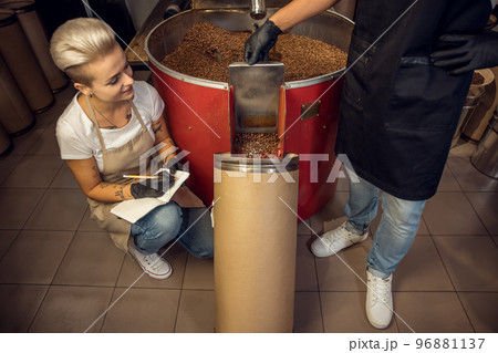 Female coffee roaster and her colleague engaged in work Female coffee roaster and her colleague engaged in work 96881137
