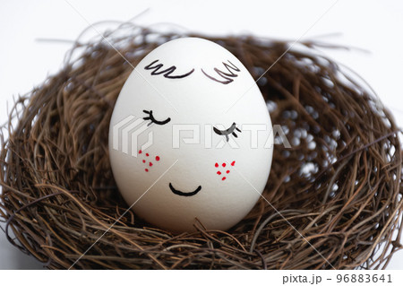 Close up of a beautiful white egg in a wicker nest on a white background. Cute face with red freckles. The view is straight. Spring postcard. Happy Easter. Close up of a beautiful white egg in a wicker nest on a white background. Cute face with red freckles. The view is straight. Spring postcard. Happy Easter. 96883641
