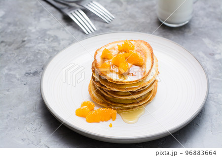 Delicious homemade pancakes with tangerines and honey, glass of milk on a plate on the table Delicious homemade pancakes with tangerines and honey, glass of milk on a plate on the table 96883664