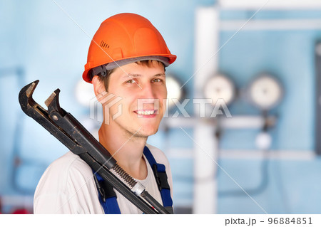 Positive industrial plumber or worker in helmet holds large adjustable wrench on his shoulder and Positive industrial plumber or worker in helmet holds large adjustable wrench on his shoulder and 96884851