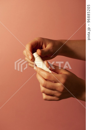 A girl opens a white tube of cream. Peach background. 96885205