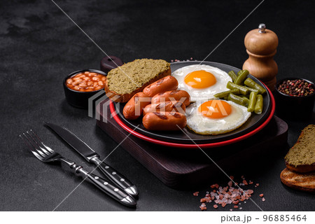 Tasty English breakfast of fried eggs, beans, asparagus, sausages with spices and herbs Tasty English breakfast of fried eggs, beans, asparagus, sausages with spices and herbs 96885464