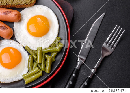 Tasty English breakfast of fried eggs, beans, asparagus, sausages with spices and herbs Tasty English breakfast of fried eggs, beans, asparagus, sausages with spices and herbs 96885474