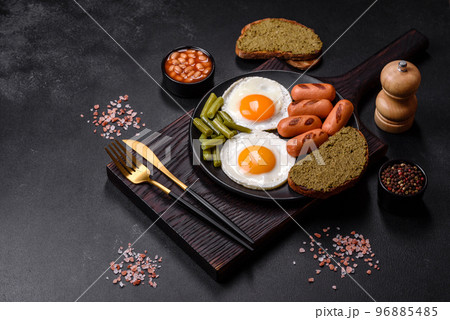 Tasty English breakfast of fried eggs, beans, asparagus, sausages with spices and herbs Tasty English breakfast of fried eggs, beans, asparagus, sausages with spices and herbs 96885485