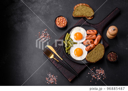 Tasty English breakfast of fried eggs, beans, asparagus, sausages with spices and herbs 96885487
