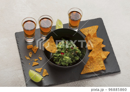 Nachos chips with guacamole and dark tequila or whiskey shots Nachos chips with guacamole and dark tequila or whiskey shots 96885860