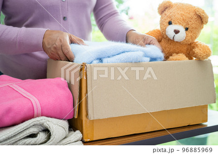 Holding clothing donation box with used clothes and doll at home to support help for poor people in the world. 96885969