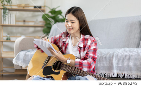 Asian woman specializes in music is composing the lyrics and melody for the opening of a new single, Using imagination and concentration in creating music, acoustic guitar, Creation of music notes. 96886245