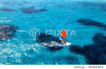 Aerial view of windsurfer on blue sea at sunny summer day Aerial view of windsurfer on blue sea at sunny summer day 96886866