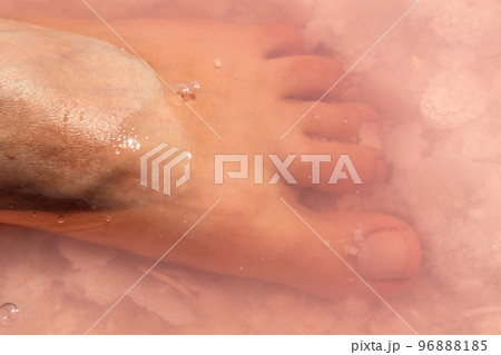 Woman foot in salt flakes in pink water, spa 96888185