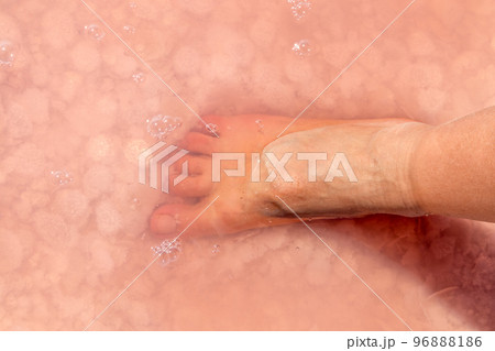 Woman foot in salt flakes in pink water, spa 96888186