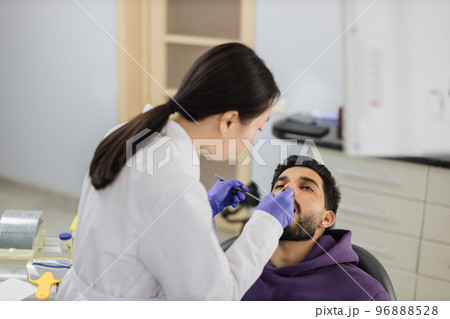 Asian dentist examines the oral cavity of young bearded handsome man Asian dentist examines the oral cavity of young bearded handsome man 96888528