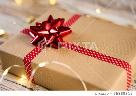 Above view of festive gift box wrapping in craft paper with festive ribbons and bow. Present for Christmas holidays on wooden background with bokeh lights 96889315