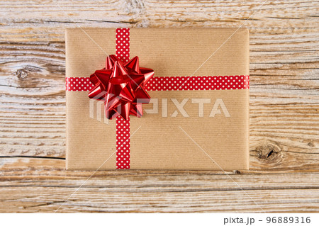 Above view of festive gift box wrapping in craft paper with festive ribbons and bow. Present for Christmas holidays on wooden background 96889316