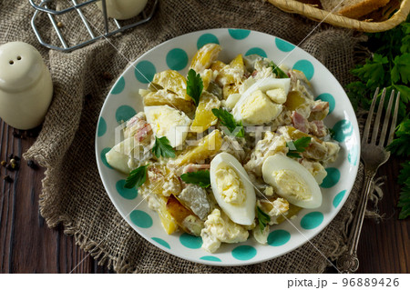 Salad with baked potatoes, pickled cucumber, egg and smoked turkey on a festive table in a rustic style. 96889426