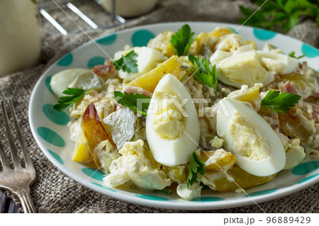Salad with baked potatoes, pickled cucumber, egg and smoked turkey close-up on a festive table in a rustic style. 96889429