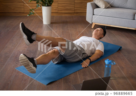 Mature korean man doing exercises for legs and abs on mat in living room interior and watching workout on laptop Mature korean man doing exercises for legs and abs on mat in living room interior and watching workout on laptop 96889665