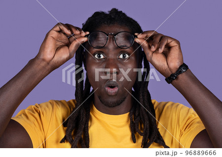 Shocked millennial african american man removing eyeglasses on purple, closeup Shocked millennial african american man removing eyeglasses on purple, closeup 96889666