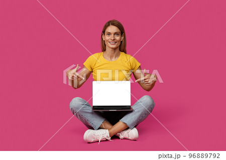 Happy adult caucasian woman blonde in casual sit on floor, point fingers at laptop with blank screen Happy adult caucasian woman blonde in casual sit on floor, point fingers at laptop with blank screen 96889792