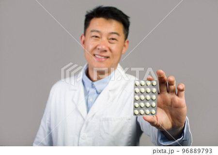 Smiling middle aged chinese male therapist in white coat showing pills, recommended medical treatment 96889793