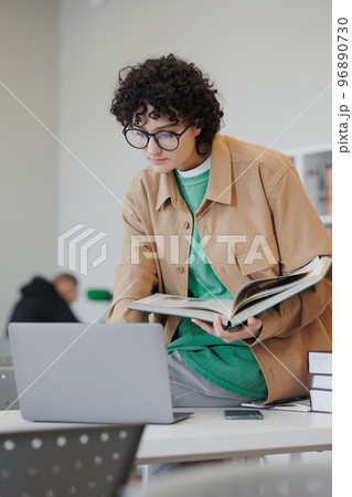 confident woman in library or coworking works laptop online, female student reads book 96890730