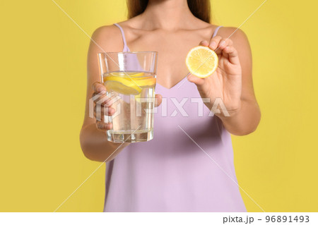 Young woman with glass of lemon water on yellow background, closeup 96891493