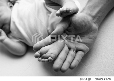 Baby feet in the hands of mother, father, older brother or sister, family. Feet of a tiny newborn close up. Little children's feet surrounded by the palms of the family. Black and white. 96893420