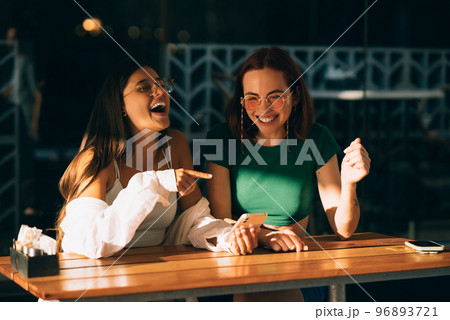 Girls using smartphones while sitting and pointing finger Girls using smartphones while sitting and pointing finger 96893721
