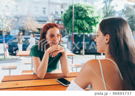Two pretty girlfriends talking while sitting in a bar outdoors 96893737