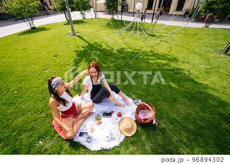 Two women having picnic together, sitting on the plaid 96894302