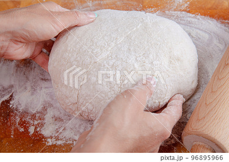 Closeup of hands prepare raw dough on wooden board sprinkled with flour with rolling pin for pizza Closeup of hands prepare raw dough on wooden board sprinkled with flour with rolling pin for pizza 96895966