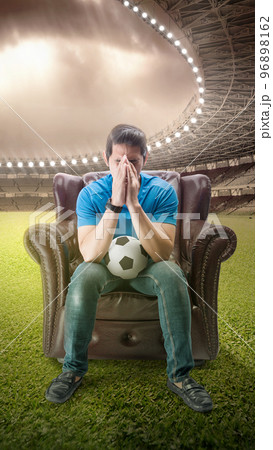 Asian man with the ball sitting on the couch with a disappointed expression 96898162
