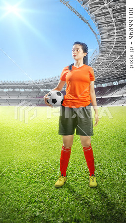 Asian football player woman in a orange jersey standing with the ball 96899100