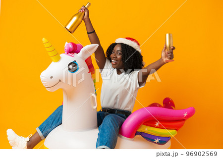 African woman sitting on rainbow unicorn float wearing santa claus hat in studio 96902569