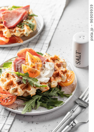 Cheese or potato savory waffles served with with tomatoes, ham and aragula with cutlery. Delisious savory breakfast 96909939