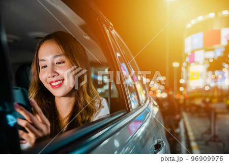Asian businesswoman working late commuting from office in Taxi backseat with mobile phone in city at night after late work, Happy beautiful woman texting smartphone sitting car back seat in urban 96909976