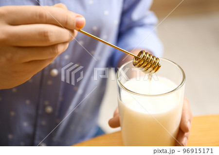 Woman adding honey to milk at table, closeup Woman adding honey to milk at table, closeup 96915171