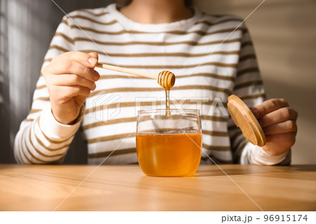 Woman with honey and dipper at wooden table, closeup Woman with honey and dipper at wooden table, closeup 96915174