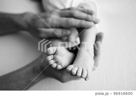 Baby feet in the hands of mother, father, older brother or sister, family. Feet of a tiny newborn close up. Little children's feet surrounded by the palms of the family. Black and white. Baby feet in the hands of mother, father, older brother or sister, family. Feet of a tiny newborn close up. Little children's feet surrounded by the palms of the family. Black and white. 96916600