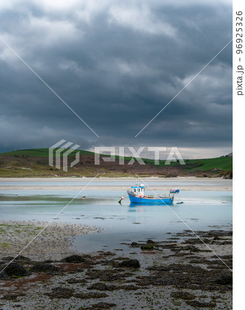 A small old fishing boat is anchored, shallow water at low tide on a cloudy day. A small old fishing boat is anchored, shallow water at low tide on a cloudy day. 96925326